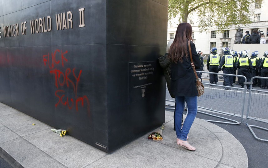 Police corral protesters behind expletive graffiti spray painted onto a war memorial.
