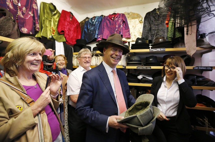 The leader of the United Kingdom Independence Party (UKIP) Farage tries on hats with shop owner Barwick during a visit to her small vintage clothing shop which has expressed its support for the party, in Canterbury southern England